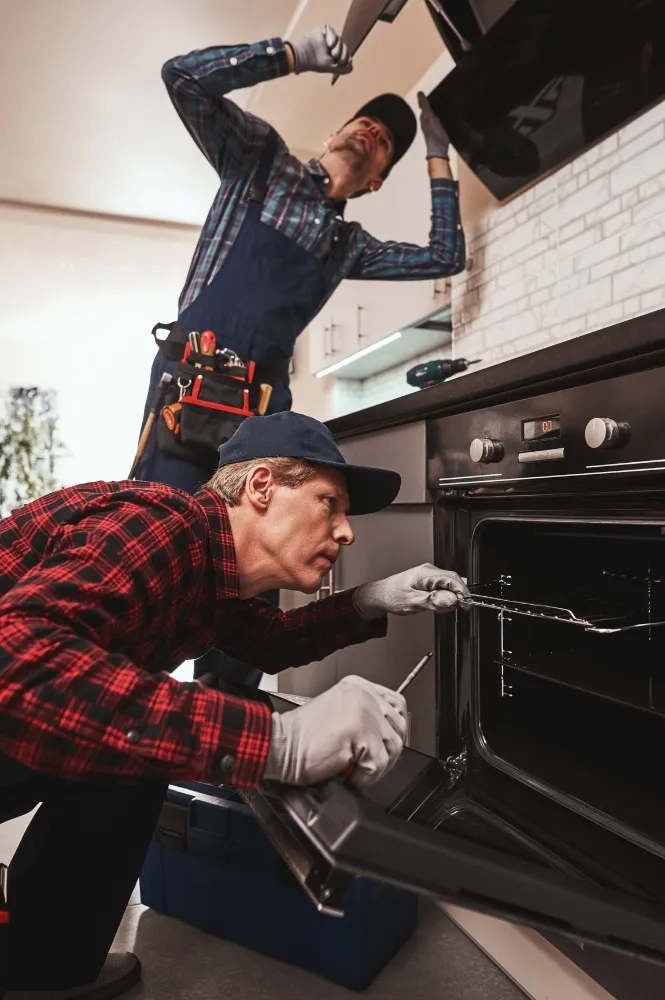 Technicians repairing a commercial cooking range in a kitchen, focusing on detailed appliance maintenance.