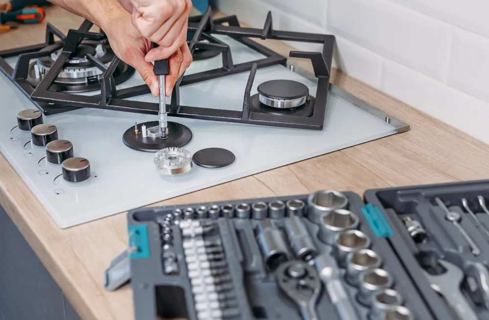 Technician repairing a gas stove burner using professional tools as part of a commercial cooking range repair service.