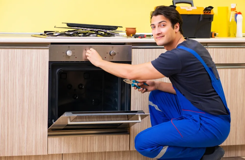 Technician smiling while repairing the oven section of a commercial cooking range in a kitchen.
