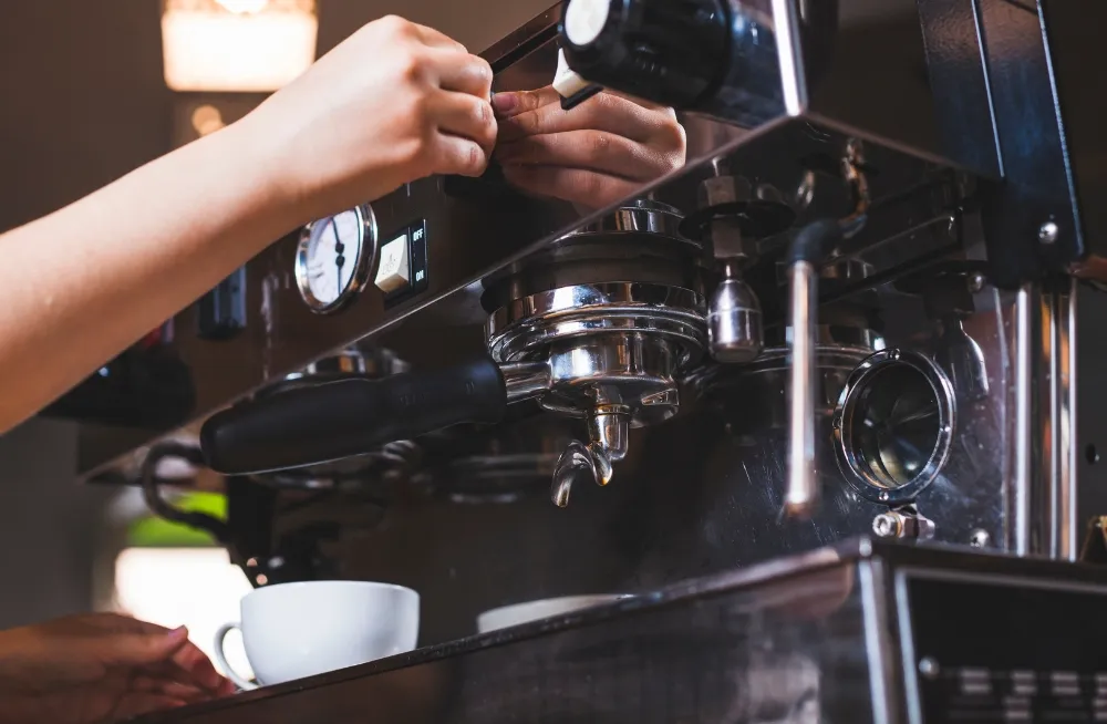 Technician adjusting a professional espresso machine with a coffee cup ready, showcasing timely commercial coffee maker repair services