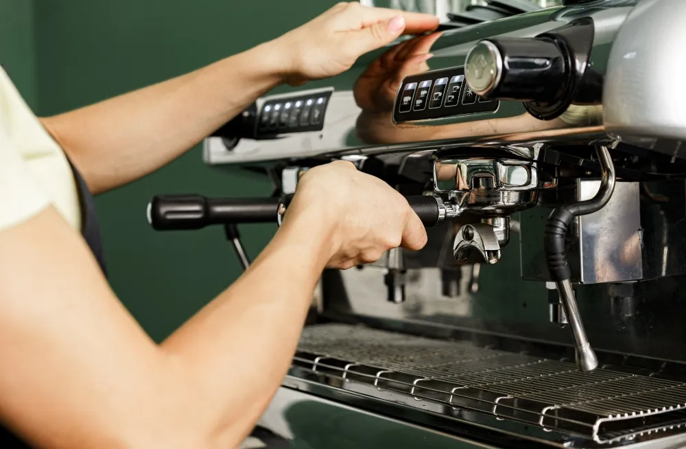 A professional technician inspecting and operating a commercial espresso machine, focusing on the portafilter and control buttons in a cafe setting.