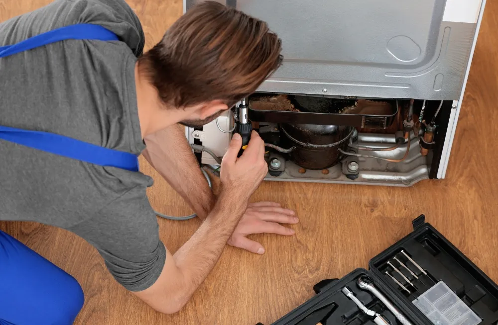 Technician repairing a refrigerator with tools nearby.