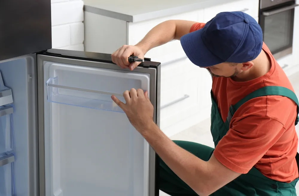 Technician repairing an open refrigerator in a kitchen setting.