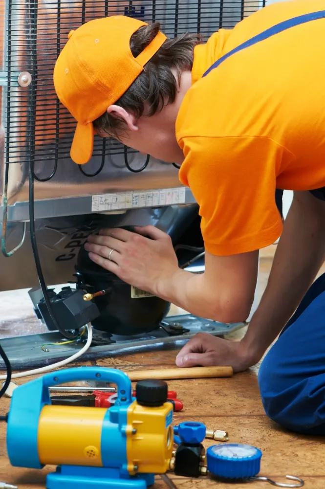 Technician in Dubai repairing a refrigerator with tools.