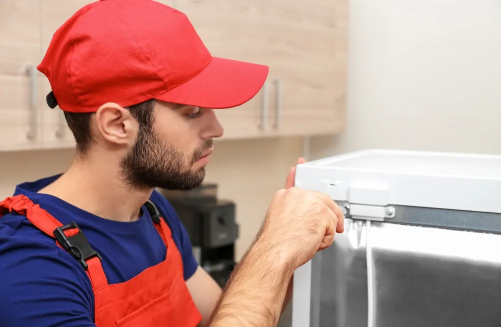 Technician in Dubai repairing a white refrigerator in a modern kitchen.