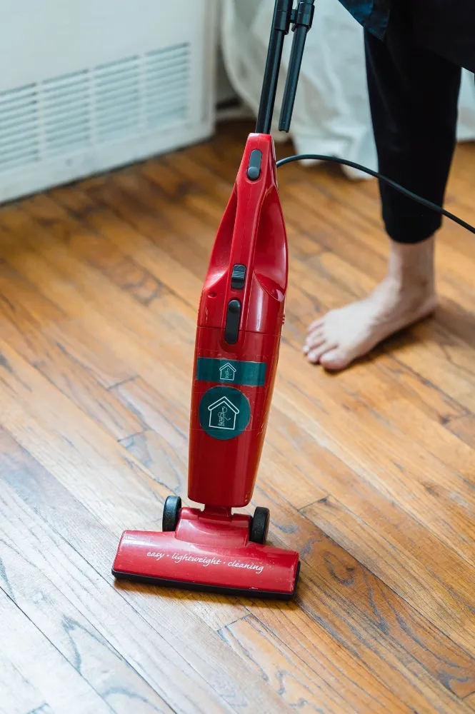 Red stick vacuum cleaner on a polished wooden floor, showcasing its easy, lightweight cleaning features. Ideal for home use. Vacuum Cleaner Repair Dubai