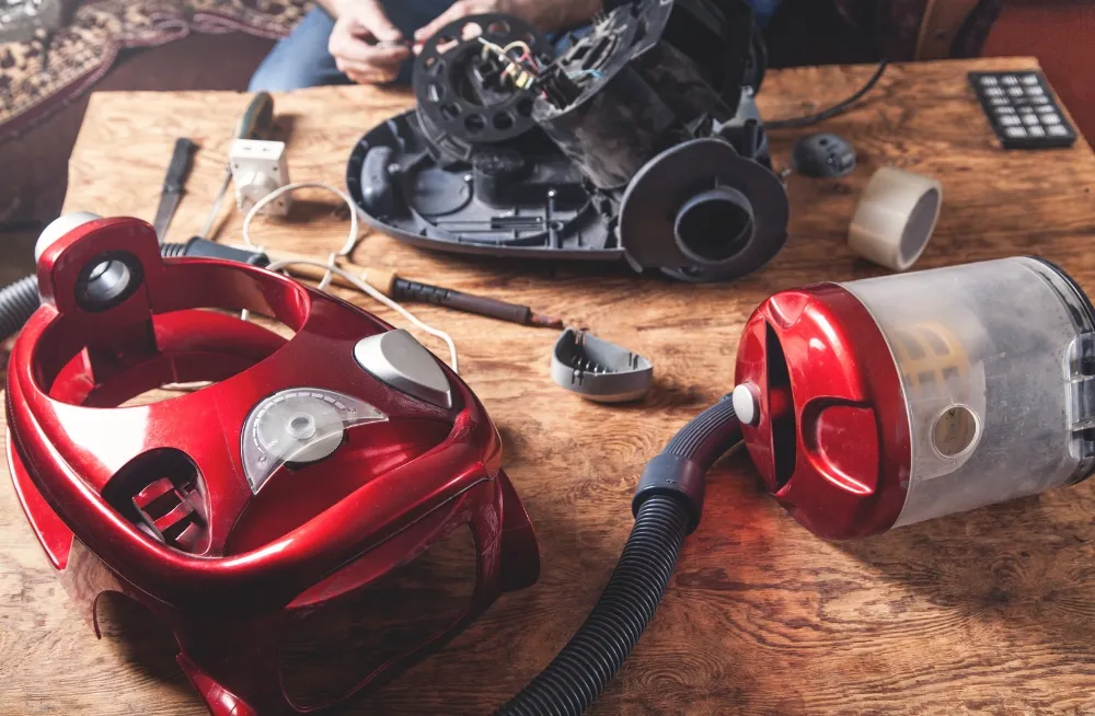 Disassembled red vacuum cleaner parts on a wooden table with tools, highlighting repair and maintenance. Vacuum Cleaner Repair Dubai - PrimeProTechnical.