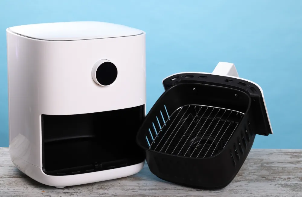 Modern white Henny Penny air fryer with a black cooking basket featuring a metal grill rack, placed on a light wooden surface with a blue background in Dubai.