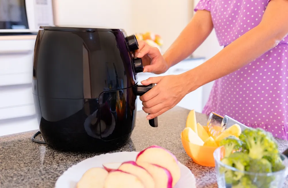 Person interacting with a black Henny Penny air fryer on a granite countertop, showcasing its control knobs and handle, ideal for repair services in Dubai.