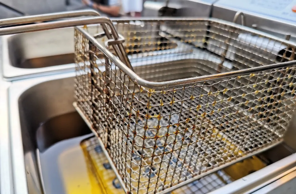 Close-up of a stainless steel deep-frying basket with oil residue, positioned over commercial fryer tanks, ideal for Henny Penny fryer repair services in Dubai.