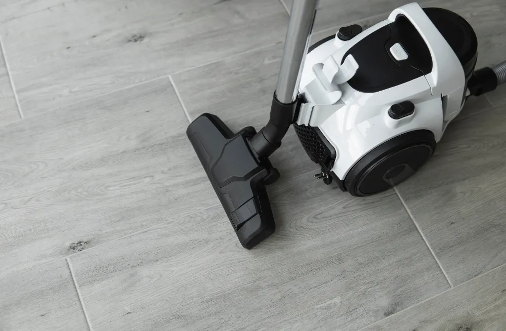 White vacuum cleaner with tools and a dustbin assembly on a wooden surface. Vacuum Cleaner Repair Dubai