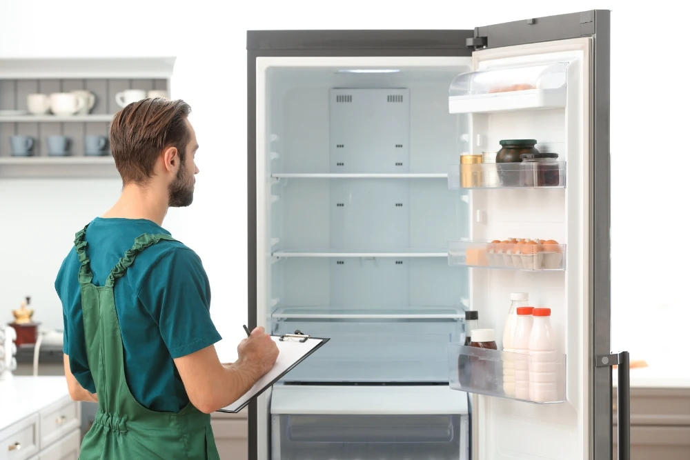 Technician checking refrigerator cooling system in home kitchen