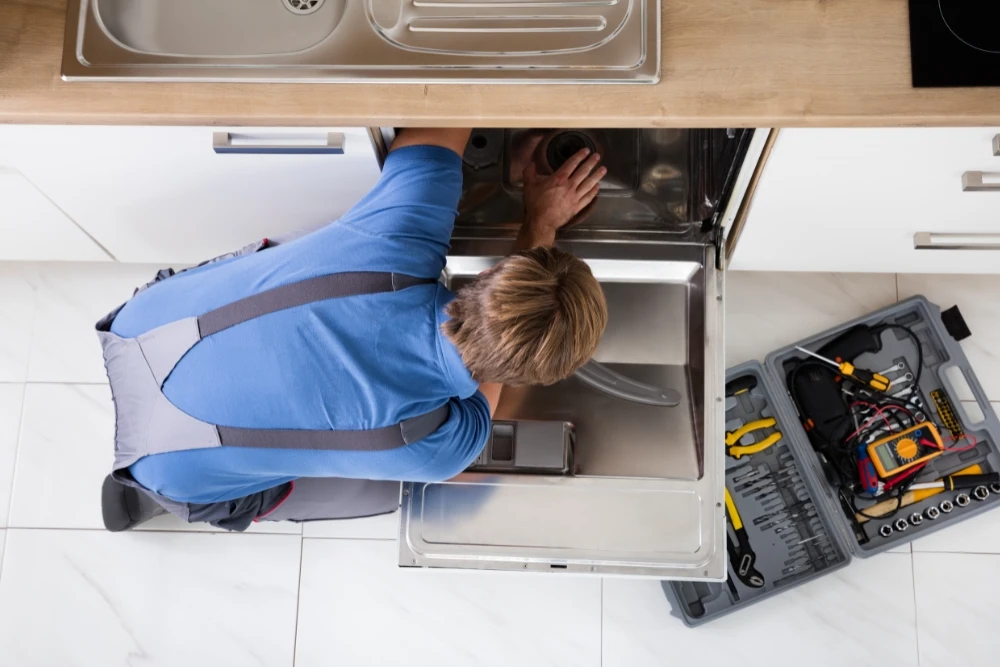 A skilled technician inspecting and repairing a dishwasher with professional tools in a residential kitchen.
