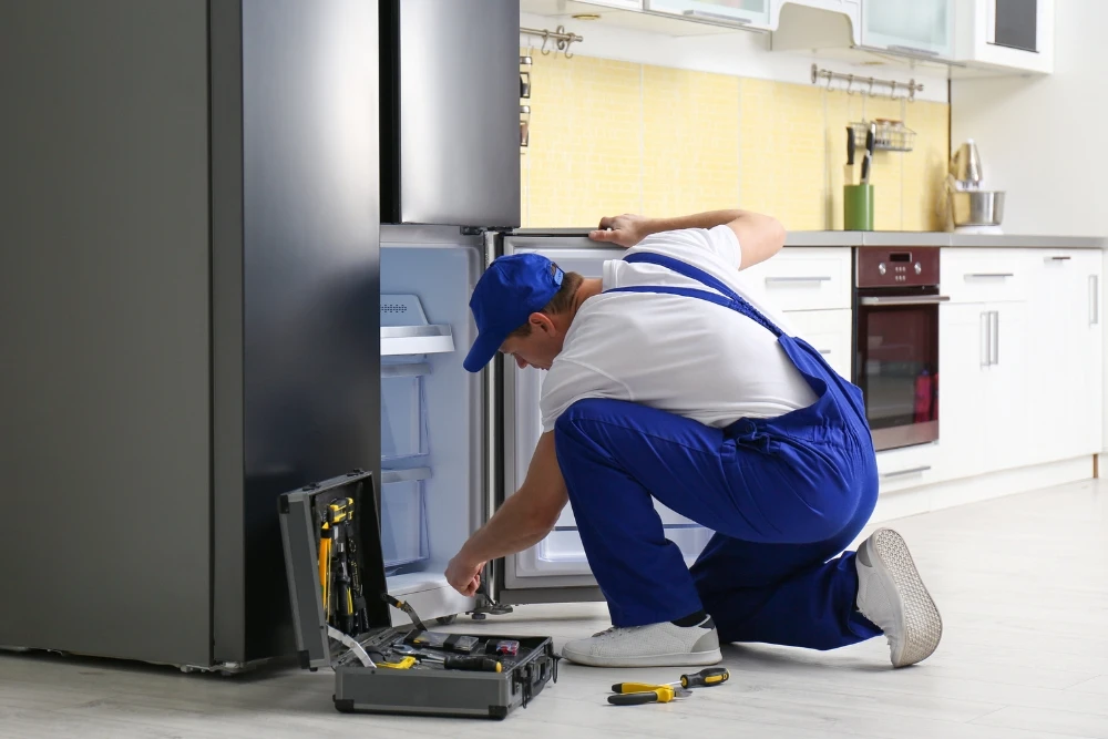 Certified appliance repair technician performing refrigerator maintenance and repair service.