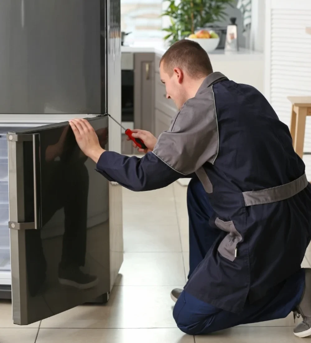 Professional refrigerator repair technician repairing a double-door fridge in a modern home kitchen.
